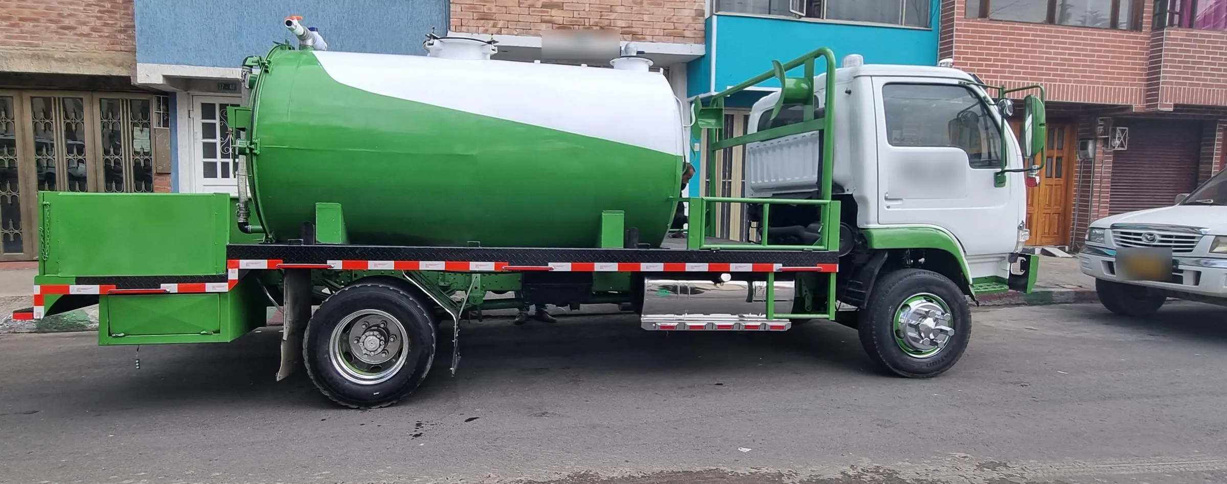 Camión tipo vactor con tanque de vacío verde y blanco, visto de perfil en la calle